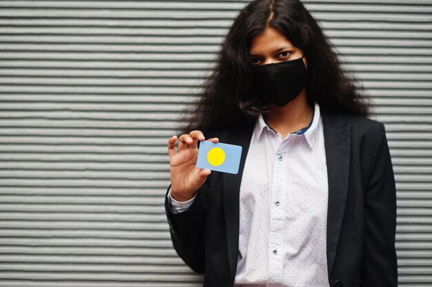 Asian woman at formal wear and black protect face mask hold Palau flag at hand against gray background Coronavirus at country concept