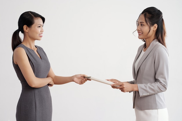 Free photo asian woman giving document folder to her female boss in business suit at work