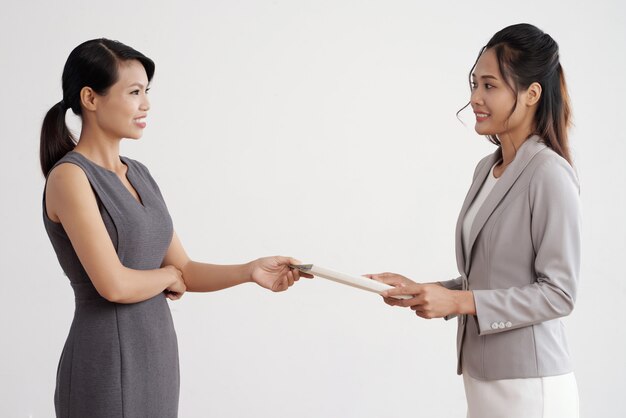 Asian woman giving document folder to her female boss in business suit at work