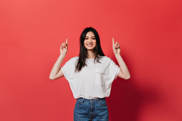 Asian woman in great mood is showing her fingers up to place for text on red wall