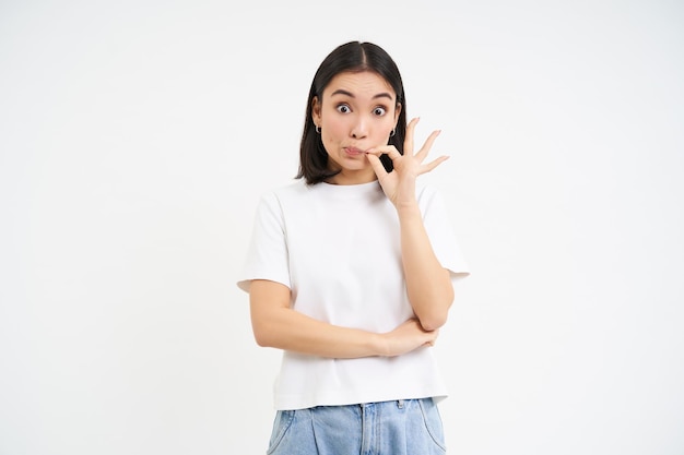 Free photo asian woman hears gossips and zips her mouth seal lips to keep promise stands over white background