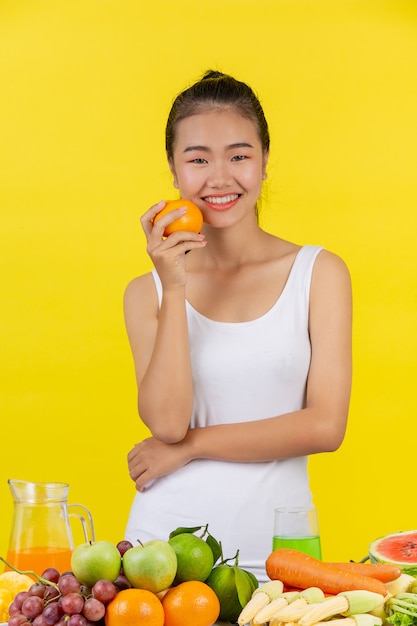 Asian woman Hold oranges with the right hand, and on the table there are many fruits.