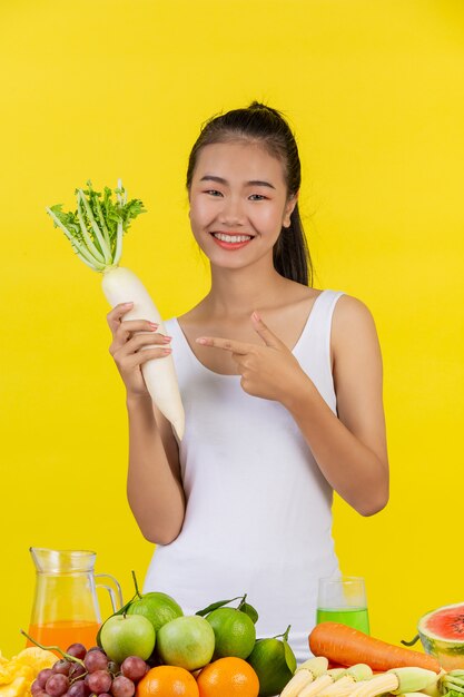 Asian woman Hold the radish with your right hand and on the table there are many fruits.