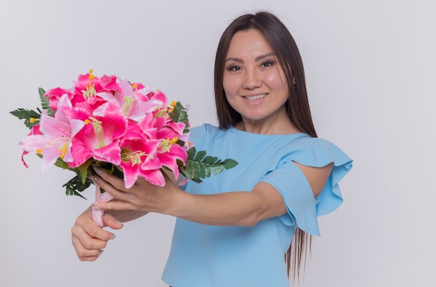 Asian woman holding bouquet of flowers looking happy and cheerful celebrating international women's day standing over white wall