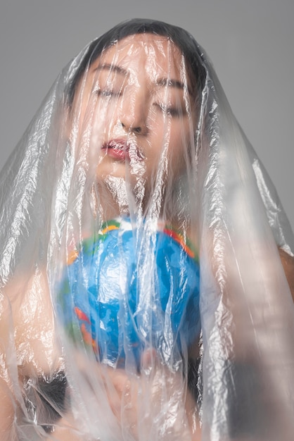 Asian woman holding an earth globe while being covered in plastic