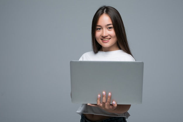 Asian woman holding laptop computer while looking at the camera over gray background