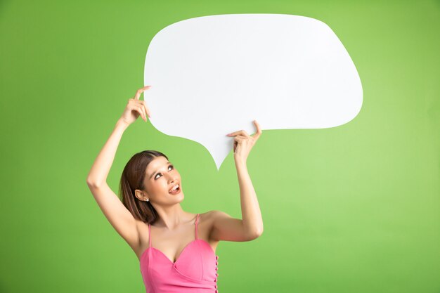 Asian woman holding and looking up to speech bubble with empty space for text on green 