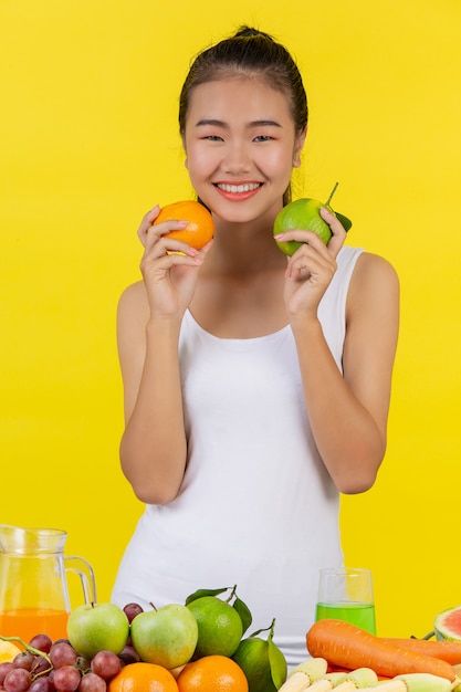 Азиатская женщина держит апельсины с обеих сторон, а на столе много фруктов.