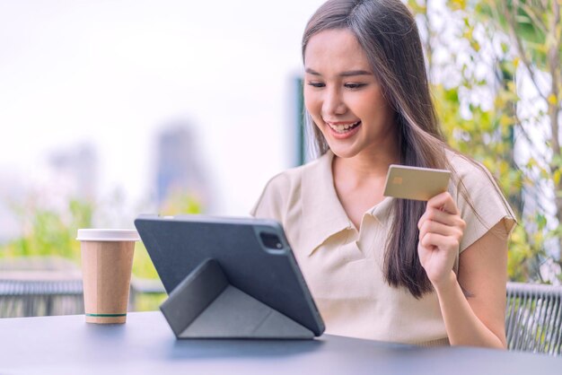 アジアの女性がオンラインで購入し、クレジットカードで支払います屋外のカフェに座って週末の休暇を楽しんでいる女性スマートフォンでオンラインショッピングをし、クレジットカードでモバイル決済を行っています