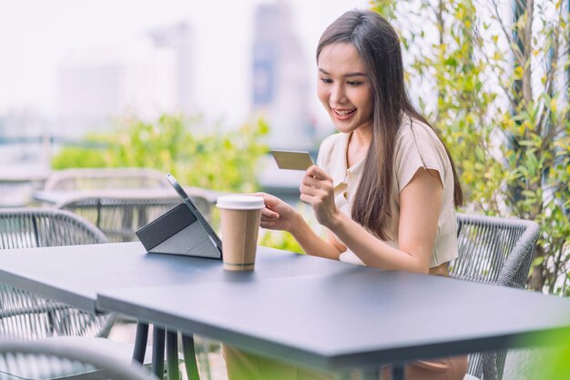 아시아 여성이 온라인으로 구매하고 신용카드로 결제하고 있습니다. 여성은 야외 카페에 앉아 주말 휴가를 즐기고 있습니다. 스마트폰으로 온라인 쇼핑을 하고 신용카드로 모바일 결제를 하고 있습니다
