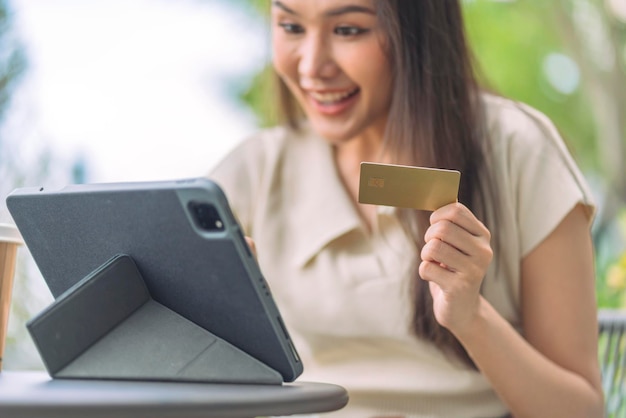 Donna asiatica sta acquistando online e pagando con carta di creditofemmina seduta al bar all'aperto godendosi le vacanze del fine settimana shopping online su smartphone ed effettuare pagamenti mobili con carta di credito