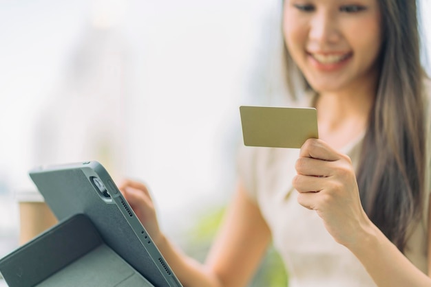 アジアの女性がオンラインで購入し、クレジットカードで支払います屋外のカフェに座って週末の休暇を楽しんでいる女性スマートフォンでオンラインショッピングをし、クレジットカードでモバイル決済を行っています