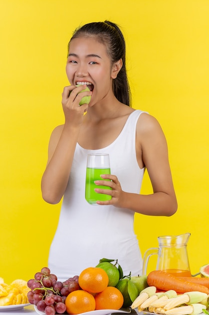 An Asian woman is going to eat a green apple. And hold a glass of apple juice.