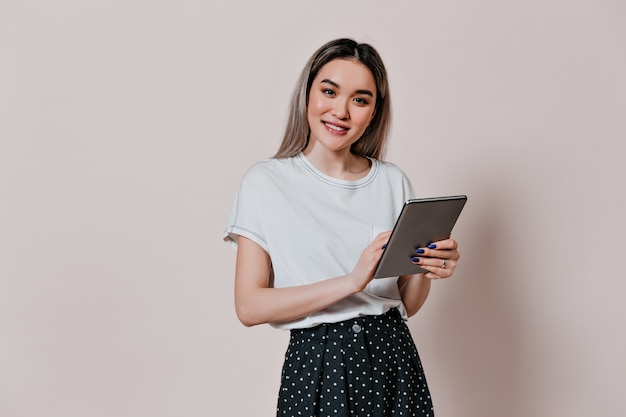 Asian woman in light t-shirt smiles and holds tablet