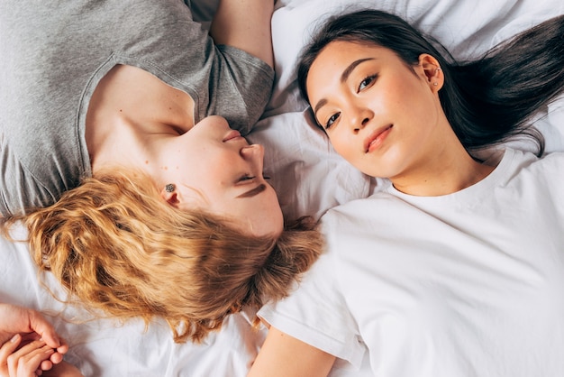 Asian woman looking at camera being in bed with girlfriend