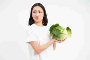 Free photo asian woman looks with disgust and dislike at cabbage hates vegetables isolated on white background