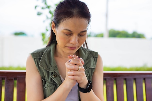 Asian woman praying morning outdoor, hands folded in prayer concept for faith, spirituality and religion, church services online concept.