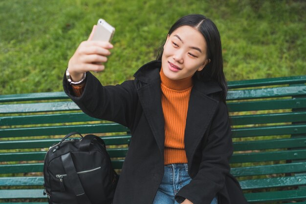 Asian woman taking selfie with phone.