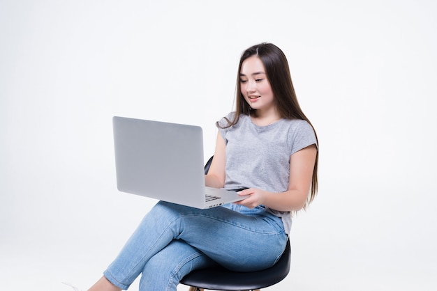 Asian woman talking on the phone and looking at a laptop while sitting on a chair. A working woman sat with her legs crossed confidently.