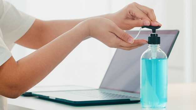 Asian woman using alcohol gel hand sanitizer wash hand before open laptop for protect coronavirus. Female push alcohol to clean for hygiene when social distancing stay at home and self quarantine time