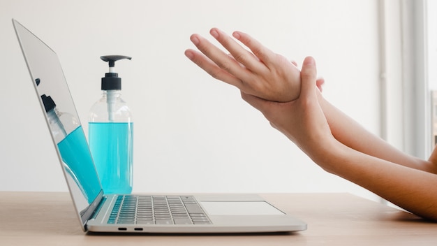 Asian woman using alcohol gel sanitizer wash hand before work on laptop for protect coronavirus. female push alcohol to clean for hygiene when social distancing stay at home and self quarantine time.