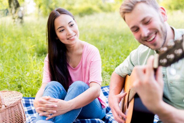 Asian woman watching man playing guitar