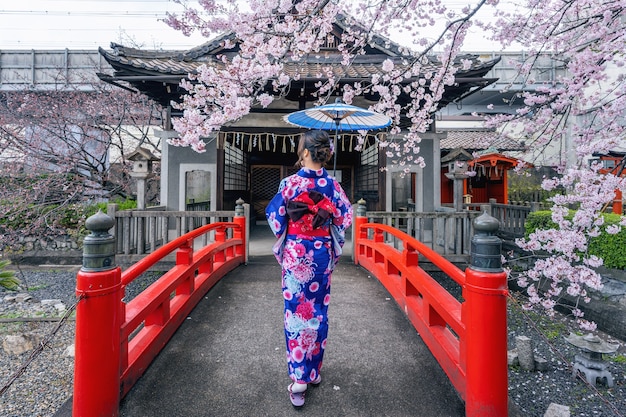 春に日本の伝統的な着物と桜を身に着けているアジアの女性、日本の京都寺院。