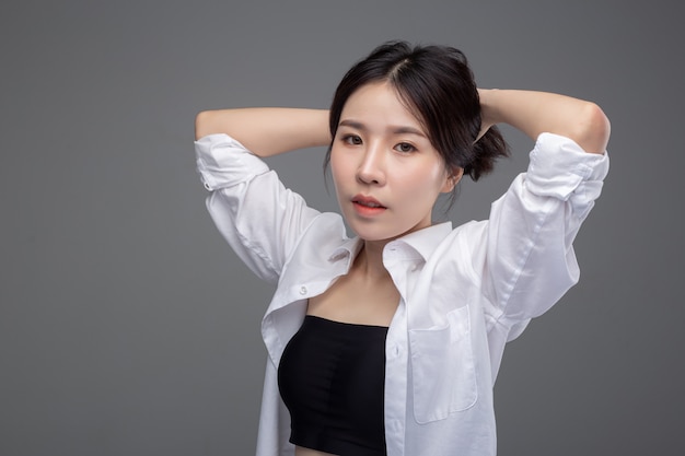 아시아 여자는 흰 셔츠를 입고 손은 그녀의 머리를 만집니다.