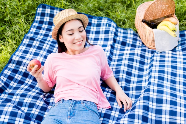Asian woman with apple lying on plaid