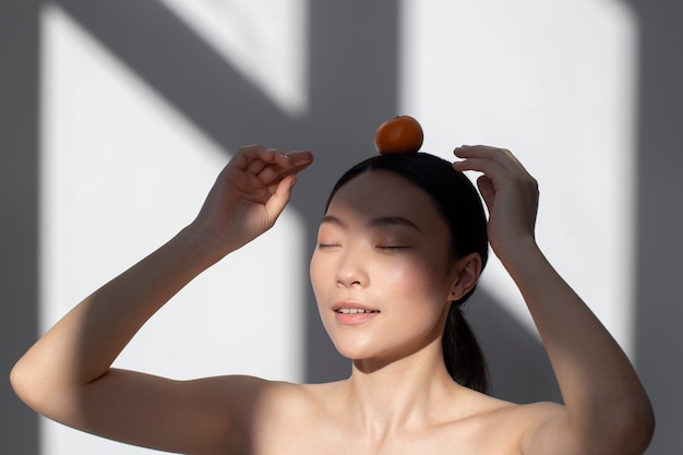 Asian woman with perfect skin posing with orange on head