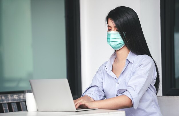 コワーキングスペースで医療マスクを着用しながらラップトップに取り組んでいるアジアの女性新しい通常のライフスタイル社会的距離