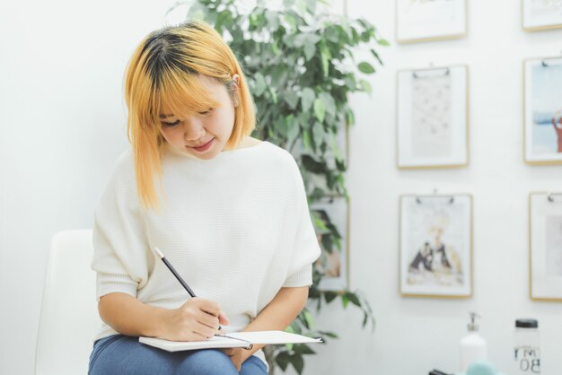 アジアの女性がショッピングリストをメモ帳に書いています。