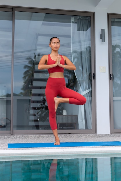Donna asiatica fare yoga fuori dalla villa in piscina donna in abbigliamento sportivo rosso fa yoga pone sul tappeto