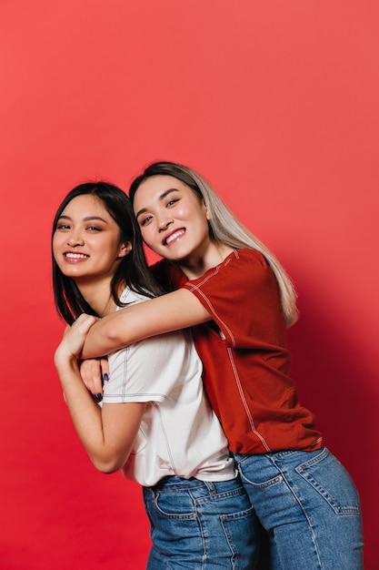 Asian womans in white and red t-shirts posing on isolated wall