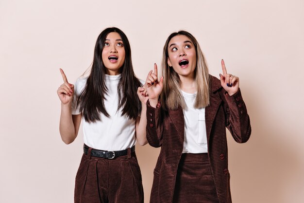 Asian women look up in surprise and point their fingers at place for text on beige wall