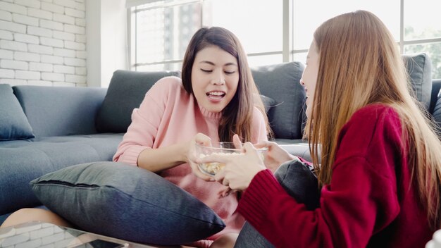베개 싸움을하고 집에서 거실에서 룸메이트 친구의 그룹에서 팝콘을 먹는 아시아 여성