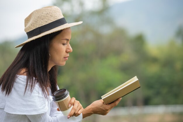 아시아 여성은 공원에서 책을 읽고 커피를 마신다.