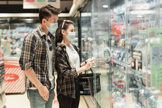 コロナウイルスの発生の中で冷凍食品を買い物するために選択する保護マスクスタンドのアジアの若いカップル
