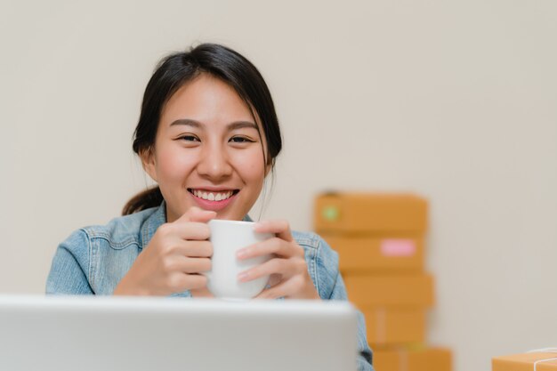 Asian young entrepreneur business woman owner of SME online checking product on stock save to computer and drinking coffee working at home.