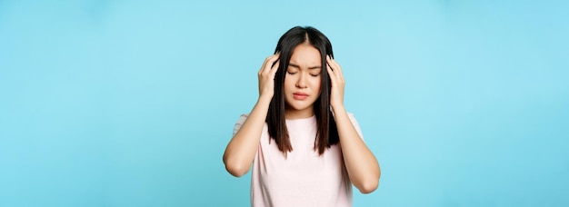 Free photo asian young girl with headache massaging her head with troubled face expression painful migraine sta