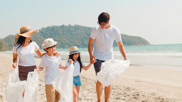 Asian young happy family activists collecting plastic waste and walking on beach. asia volunteers help to keep nature clean up garbage. concept about environmental conservation pollution problems.