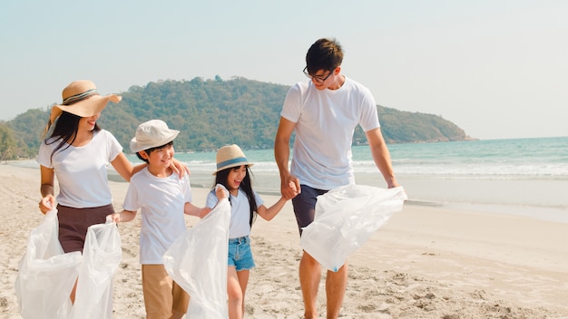 Asian young happy family activists collecting plastic waste and walking on beach. Asia volunteers help to keep nature clean up garbage. Concept about environmental conservation pollution problems.