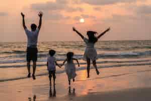 自由亚洲年轻幸福的家庭照片在海滩晚上享受假期。爸爸,妈妈和孩子一起放松跑附近海而轮廓日落。夏天旅游度假度假生活方式的概念。