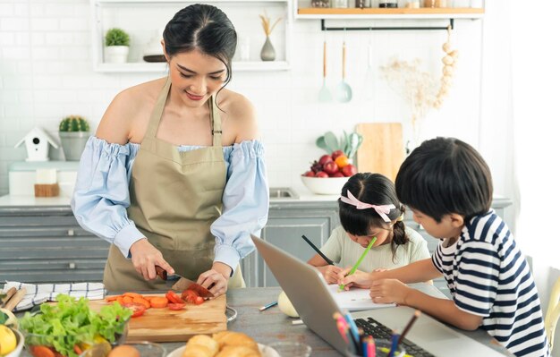 キッチンで子供を世話しながら食べ物を作るアジアの若い独身の母親