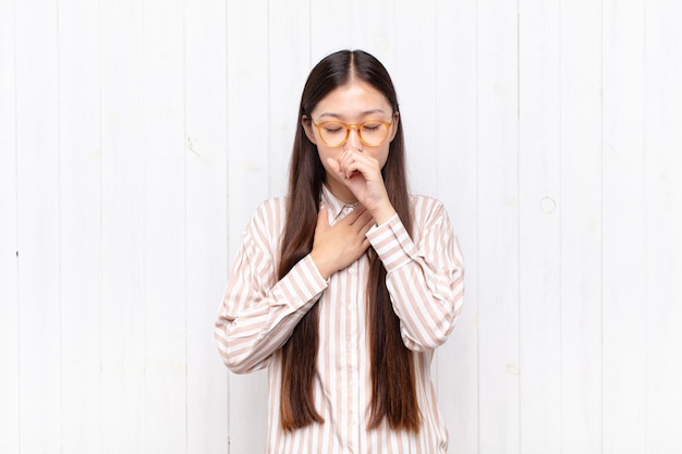 Asian young woman feeling ill with a sore throat and flu symptoms, coughing with mouth covered