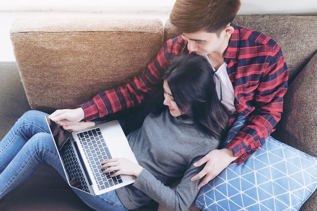 Asian young woman and handsome man sitting on couch using laptop