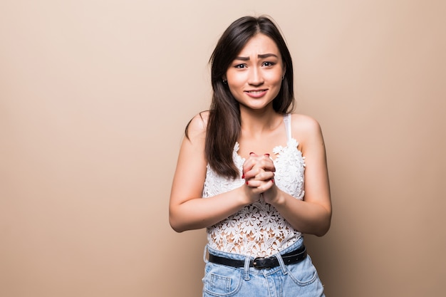 Asian young woman over isolated beige wall keeps palm together. Person asks for something