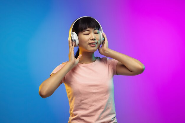 Asian young woman's portrait on gradient studio background in neon. Beautiful female model in casual style. 