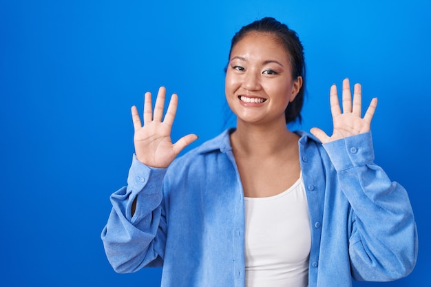 Foto gratuita giovane donna asiatica in piedi su sfondo blu che mostra e punta verso l'alto con le dita numero dieci mentre sorride fiducioso e felice.