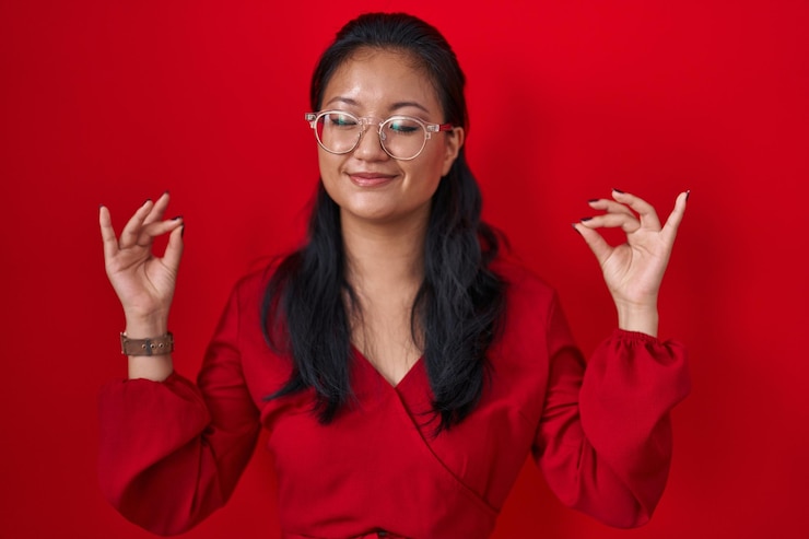 Free Photo asian young woman standing over red background relaxed and smiling with eyes closed doing meditation gesture with fingers. yoga concept.